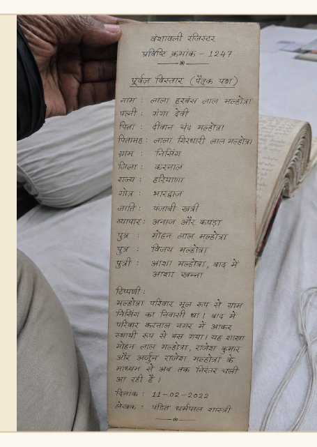 Photograph of a handwritten Hindi family-register entry, held open by the register keeper